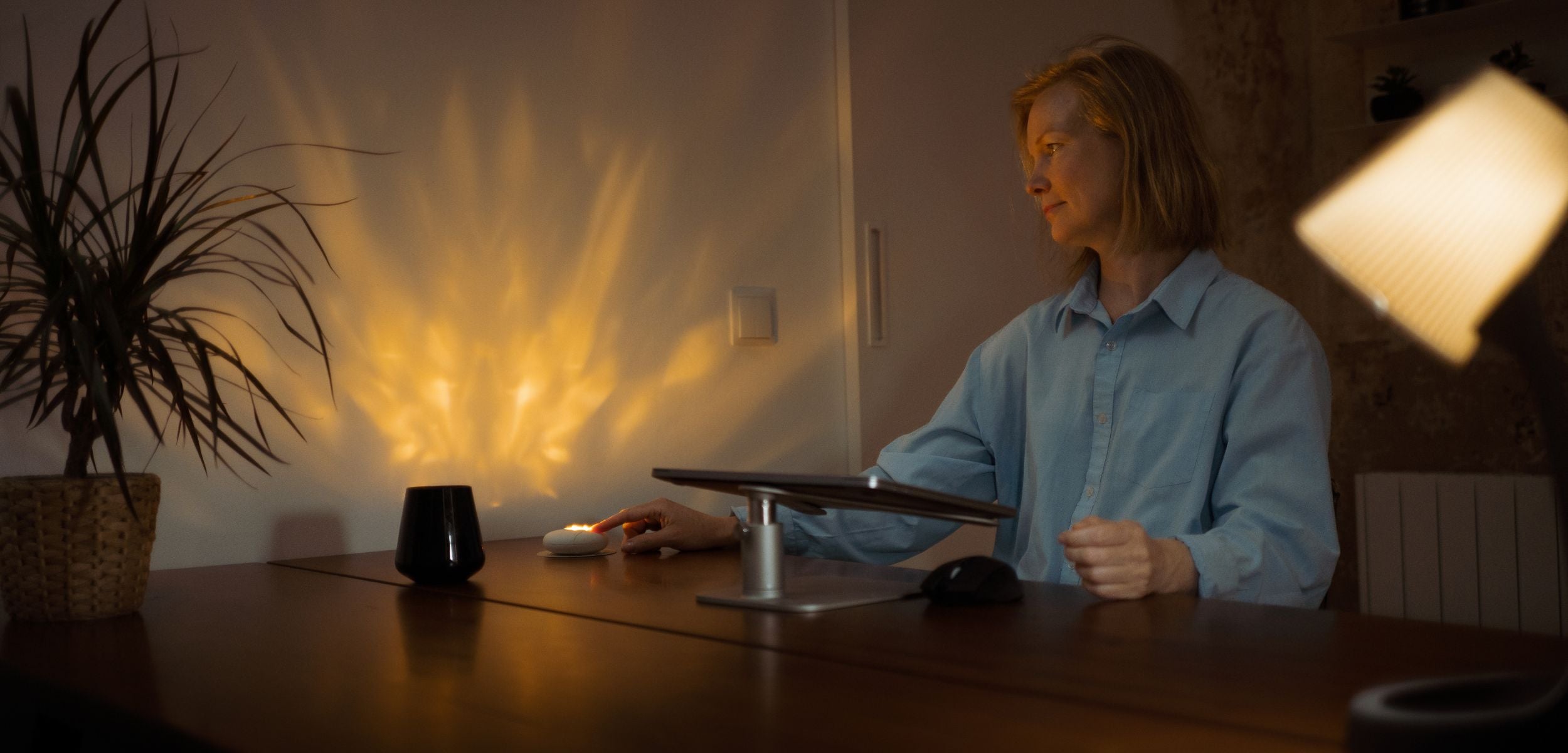 Eine Frau sitzt am Schreibtisch und betätigt das HerzLicht. Es dient ihr als 10 Minuten Timer für eine wohlverdiente Pause.