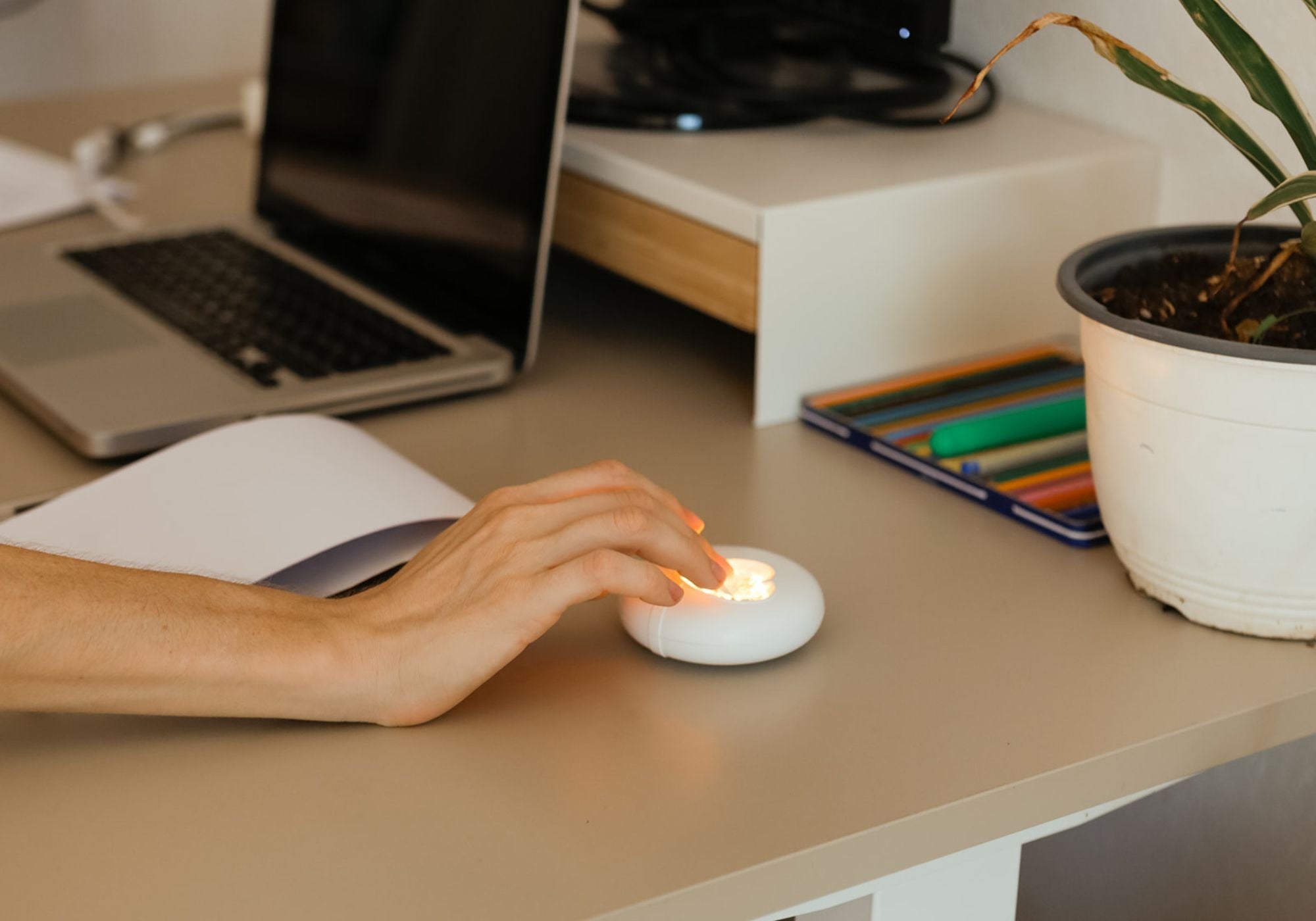 Das HerzLicht liegt neben dem Notebook auf dem Schreibtisch, und wird von einer Frauenhand gedrückt.