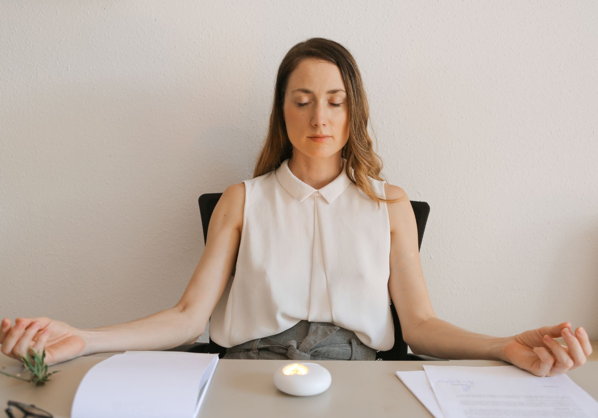 Eine Frau sitzt am Schreibtisch und meditiert. Vor ihr liegt das HerzLicht, das als 10 Minuten Timer dient.